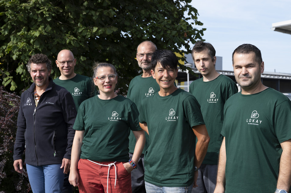 Das Team in neuer Arbeitskleidung: eine Gruppe von Menschen steht in zwei Reihen da. Sie tragen alle grüne Tshirts mit weißem Lokay-Logo auf der Brust. Nur Ralf Lokay, der auch dabei steht, trägt eine schwarze Jacke mit weißem Lokay-Logo.
