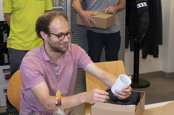 Umweltmanager Jonas Muhly packt sein Paket aus. Er hält eine Tasse in der Hand und betrachtet sie mit einem großen Lächeln.