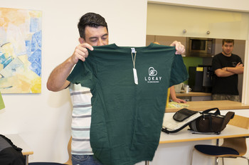 Ismail hält eins seiner neuen, dunkelgrünen Tshirt mit beiden Händen vor sich und begutachtet es. 