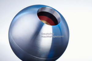 Der Deutsche Nachhaltigkeitspreis: eine silberne Kugel mit einer Einbuchtung. Dort sind schwarz-rot-goldene Streifen zu sehen. Auf der Kugel die Aufschrift "Deutscher Nachhaltigkeitspreis"